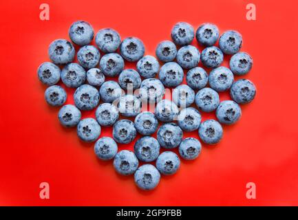 Coeur fait de bleuets frais sur fond rouge. Concept de saine alimentation. Banque D'Images