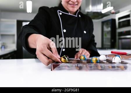 Main de la femme latine pâtissière vêtue de l'uniforme noir dans le processus de préparer de délicieux bonbons chocolats dans la cuisine au Mexique Amérique latine Banque D'Images