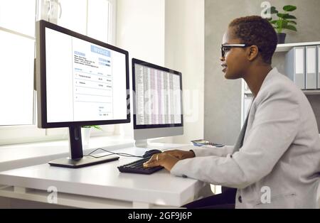 Femme comptable afro-américaine travaillant avec un logiciel pour les factures électroniques sur ordinateur. Banque D'Images