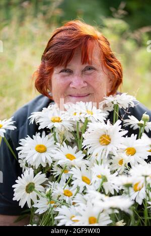 Belle femme âgée avec un bouquet de pâquerettes souriant et regardant la caméra. Banque D'Images