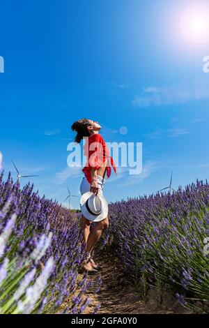 Une jeune femme se détendant dans un champ de lavande en fleur. Elle respire profondément et tourne son regard vers le haut vers les rayons chauds du soleil. Vent Banque D'Images