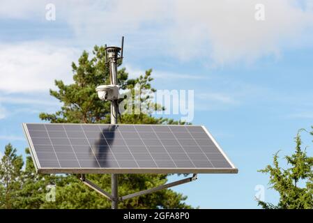 Caméra de surveillance à énergie solaire. Panneaux solaires alimentant une caméra de surveillance dans un parc urbain sur fond de ciel bleu. Sécurité et nettoyage Banque D'Images