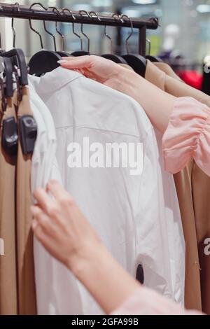 Femme magasiner dans le centre de mode, choisir de nouveaux vêtements, regarder à travers des cintres avec différents vêtements décontractés colorés sur des cintres, gros vers le haut des mains Banque D'Images