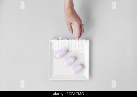 Trois eclairs sur une assiette blanche, bonbons pour un en-cas, restauration, petit déjeuner léger, une main de femme atteint pour l'assiette Banque D'Images