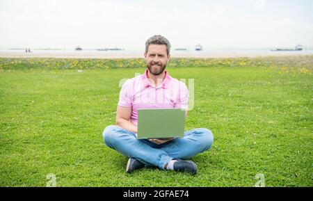 homme d'affaires heureux utilisant un ordinateur portable pour bloguer sur l'herbe verte, indépendant Banque D'Images
