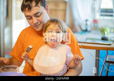 adorable bébé mange de la glace et montre la langue. père nourrissant bébé lanch Banque D'Images