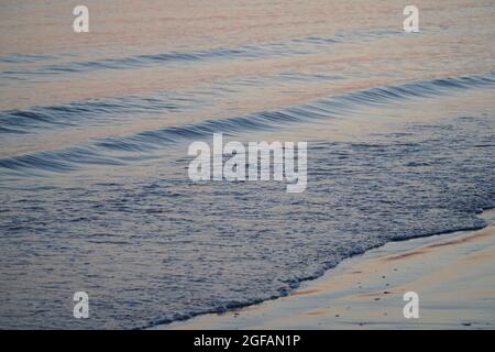 East Wittering, Royaume-Uni, 23 août 2021 : les vagues douces sur la plage de sable au crépuscule reflètent les bleus et les roses dans le ciel juste après le coucher du soleil. La mer est l'Engli Banque D'Images