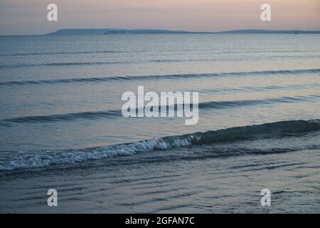 East Wittering, Royaume-Uni, 23 août 2021 : les vagues douces sur la plage de sable au crépuscule reflètent les bleus et les roses dans le ciel juste après le coucher du soleil. La mer est l'Engli Banque D'Images