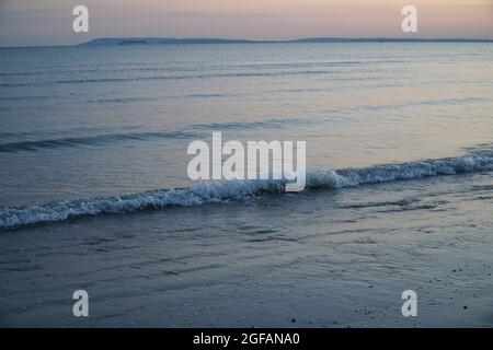 East Wittering, Royaume-Uni, 23 août 2021 : les vagues douces sur la plage de sable au crépuscule reflètent les bleus et les roses dans le ciel juste après le coucher du soleil. La mer est l'Engli Banque D'Images