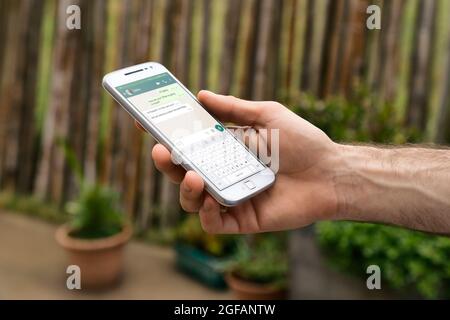 Homme avec un téléphone cellulaire blanc dans sa main. L'application WhatsApp s'affiche à l'écran. Banque D'Images