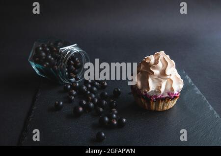 Appétissant muffin à la vanille cuit avec des raisins de Corinthe sur un plateau de service noir. Délicieux cupcake au chocolat sur un fond sombre avec des raisins de Corinthe éparpillés Banque D'Images