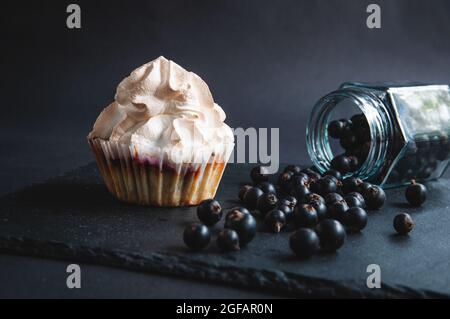 Appétissant muffin à la vanille cuit avec des raisins de Corinthe sur un plateau de service noir. Délicieux cupcake au chocolat sur un fond sombre avec des raisins de Corinthe éparpillés Banque D'Images