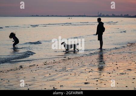 East Wittering, Royaume-Uni, 23 août 2021 : les gens et les chiens apprécient le temps sec sur la plage d'East Wittering dans West Sussex pendant que le soleil se couche sur le Solen Banque D'Images