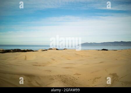 Dunes de sable menant à l'océan Pacifique à Pismo Beach, le jour nuageux de l'hiver, avec des montagnes gris ciel à l'horizon Banque D'Images
