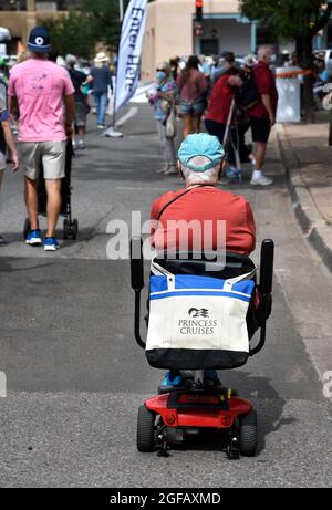 Une femme âgée conduisant un scooter motorisé avec un sac fourre-tout Princess Cruises visite un spectacle d'art en plein air à Santa Fe, Nouveau-Mexique. Banque D'Images