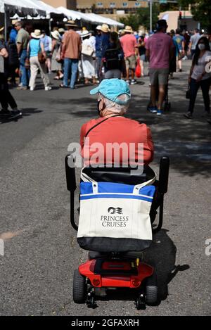 Une femme âgée conduisant un scooter motorisé avec un sac fourre-tout Princess Cruises visite un spectacle d'art en plein air à Santa Fe, Nouveau-Mexique. Banque D'Images