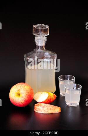 Calvados de pomme, alcool fort dans une bouteille et deux verres se tient sur un fond noir, fruits mûrs à proximité. Gros plan. Banque D'Images