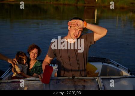 Homme adulte protégeant le visage de la lumière du soleil lors de la promenade en bateau à moteur avec la famille le jour d'été sur le lac Banque D'Images