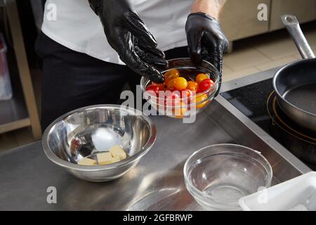 Un chef cuisinier prépare une salade dans la cuisine. Chef cuisinier qui prépare un délicieux plat dans la cuisine du restaurant. Fromage à frire dans un bol Banque D'Images