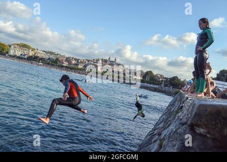 Saint-Sébastien, Espagne. 25 août 2021. Un jeune homme plonge dans l'eau de mer en effectuant un saut acrobatique à la plage de la Concha à San Sebastian.les jeunes apprécient cet été de sauter dans l'eau depuis le mur à l'extrémité de la promenade de Playa de la Concha de San Sebastian à côté de Monte Igueldo avec des sauts spectaculaires et sans le danger que les falaises de pierre offrent pour ce type de sauts. Crédit : SOPA Images Limited/Alamy Live News Banque D'Images