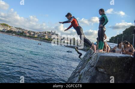 Saint-Sébastien, Espagne. 25 août 2021. Un jeune homme plonge dans l'eau de mer en effectuant un saut acrobatique à la plage de la Concha à San Sebastian.les jeunes apprécient cet été de sauter dans l'eau depuis le mur à l'extrémité de la promenade de Playa de la Concha de San Sebastian à côté de Monte Igueldo avec des sauts spectaculaires et sans le danger que les falaises de pierre offrent pour ce type de sauts. (Photo de Ramon Costa/SOPA Images/Sipa USA) crédit: SIPA USA/Alay Live News Banque D'Images