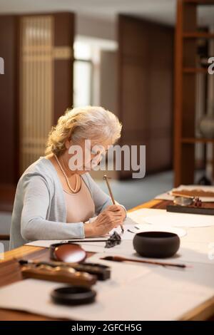 Femme sénior pratiquant la calligraphie dans l'étude Banque D'Images