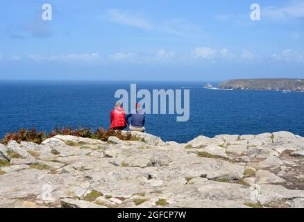 Deux personnes non identifiées assises sur les rochers au bord de la mer et bénéficiant de la vue sur la côte bretonne, France Banque D'Images