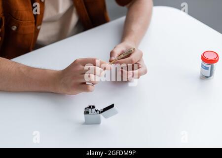 vue rognée de l'homme qui fait l'articulation avec du cannabis médical près d'un briquet sur la table Banque D'Images