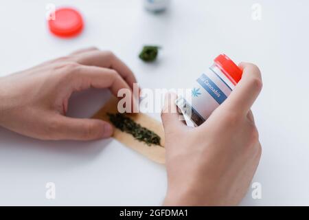 vue rognée d'un homme tenant un contenant avec des médicaments tout en faisant l'articulation avec du cannabis médical sec Banque D'Images