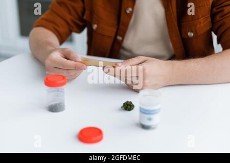 vue partielle de l'homme malade faisant joint avec du chanvre médical près des récipients sur la table Banque D'Images