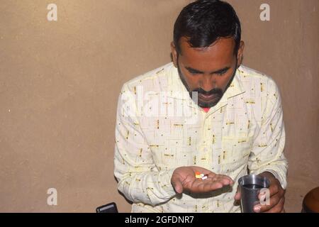 Jeune rural avec des pilules et un verre d'eau dans ses mains, il va prendre des médicaments, période Corona Banque D'Images