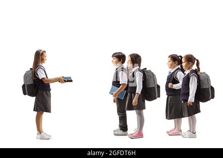 Écolière donnant des livres à un groupe de jeunes écoliers en uniformes isolés sur fond blanc Banque D'Images