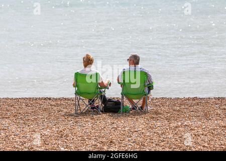 Un couple assis dans des chaises vertes sur une plage de galets au bord de la mer. Banque D'Images