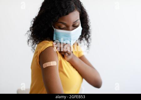 Femme afro-américaine vaccinée portant un masque facial de protection, fond gris Banque D'Images