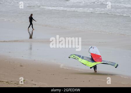 Une personne portant une planche à feuilles; c'est une planche de surf hydrofoil normalement utilisée en conjonction avec un cerf-volant pour la propulsion, fait son chemin le long de la plage Llangennith, Gower, Swansea, Royaume-Uni, vers la mer. Banque D'Images