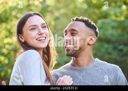 Jeune couple souriant assis dans un parc public Banque D'Images