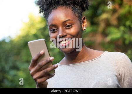 Gros plan d'une jeune femme souriante utilisant un smartphone dans le parc Banque D'Images