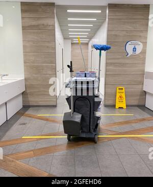 MOSCOU, Russie, mai 2021: Un chariot de nettoyage avec des balais dans des toilettes publiques vides. Sur les lignes de division du sol pour la distance sociale, le signe d'avertissement jaune nous Banque D'Images