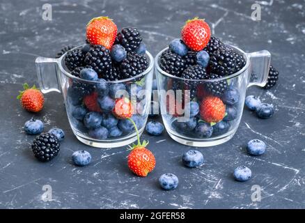 Deux verres remplis de bleuets frais, de fraises et de mûres sur une table noire. Concept de cocktail de vitamines organiques. Banque D'Images