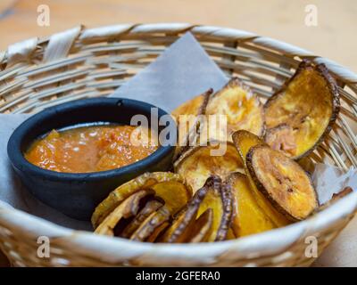 Plantain de pièces de monnaie frites et de sauce dans un bol traditionnel d'argile noire, cuisine colombienne traditionnelle. Colombie, Amérique du Sud. Banque D'Images