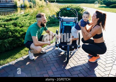 Bonne famille sportive avec un enfant près de la poussette de jogging après l'entraînement dans le parc de la ville Banque D'Images