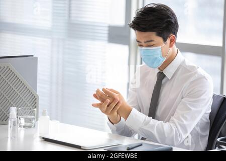 Jeune homme d'affaires utilisant l'assainisseur pour les mains dans le bureau Banque D'Images