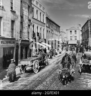 Une photographie du début du XXe siècle des acheteurs et des habitants de High Street, dans la ville de Galway. Des chariots à cheval et à âne manoeuvent autour des lignes de tramway qui descendent au centre de la rue. Banque D'Images