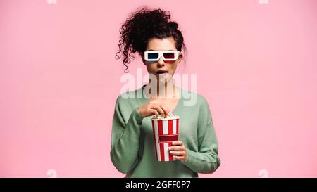 femme impressionnée dans des verres en 3d mangeant du pop-corn isolé sur rose Banque D'Images