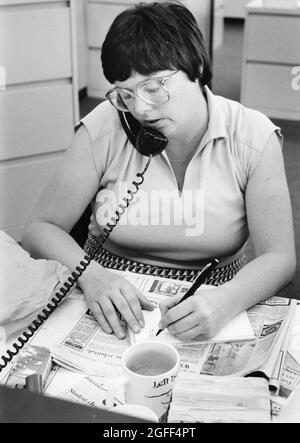 Austin Texas USA, vers 1984: Une journaliste de presse féminine interview sujet par téléphone et prend des notes à son bureau dans la salle de presse du quotidien, Austin homme d'État américain. ©Bob Daemmrich Banque D'Images