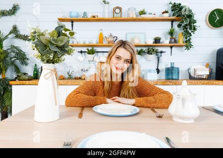 Jeune femme assise à la table de cuisine devant une plaque vide et regarde directement dans la caméra. Banque D'Images