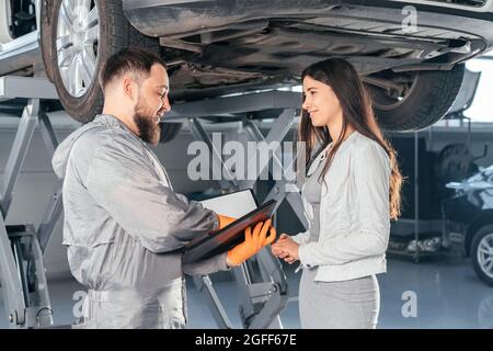 Presse-papiers de maintien Auto Mechanic discutant avec une cliente en atelier au centre de réparation automobile. Qualité de service Banque D'Images