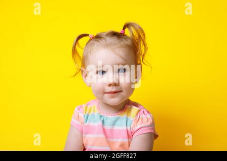 petite fille caucasienne souriant et regardant l'appareil photo sur fond jaune Banque D'Images