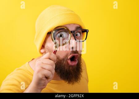homme choqué avec loupe sur fond jaune Banque D'Images