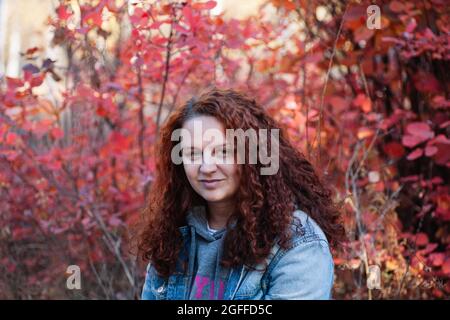 concept portrait de femme en gros plan. Femme curvy aux cheveux bruns en forêt d'automne avec buisson rouge sur fond Banque D'Images